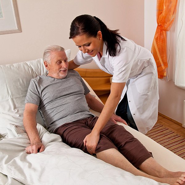 Caregiver helping elderly man out of bed