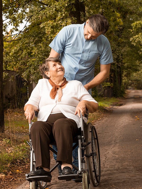 Caregiver pushing elderly woman on wooded path