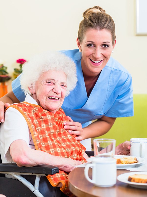Elderly lady in wheelchair at dining room table with nurse