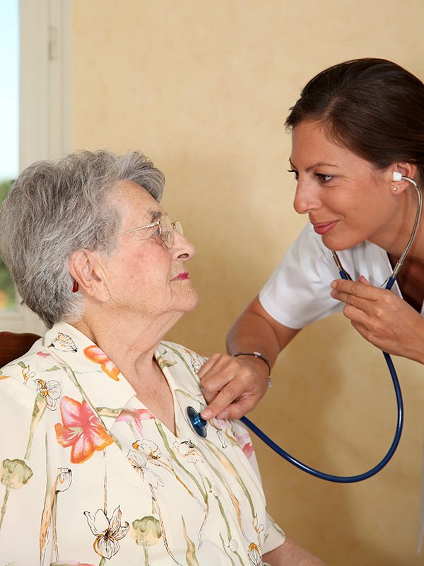 Caregiver checking elderly woman's heart